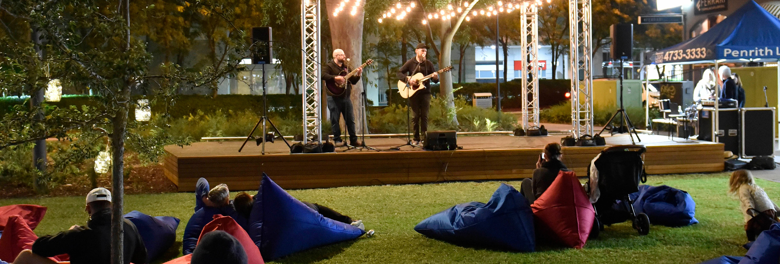 Audience listening to performers on outdoor stage at night