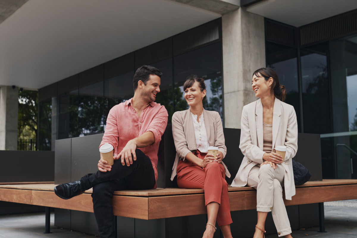 Workers sitting outside an office building drinking takeaway coffee