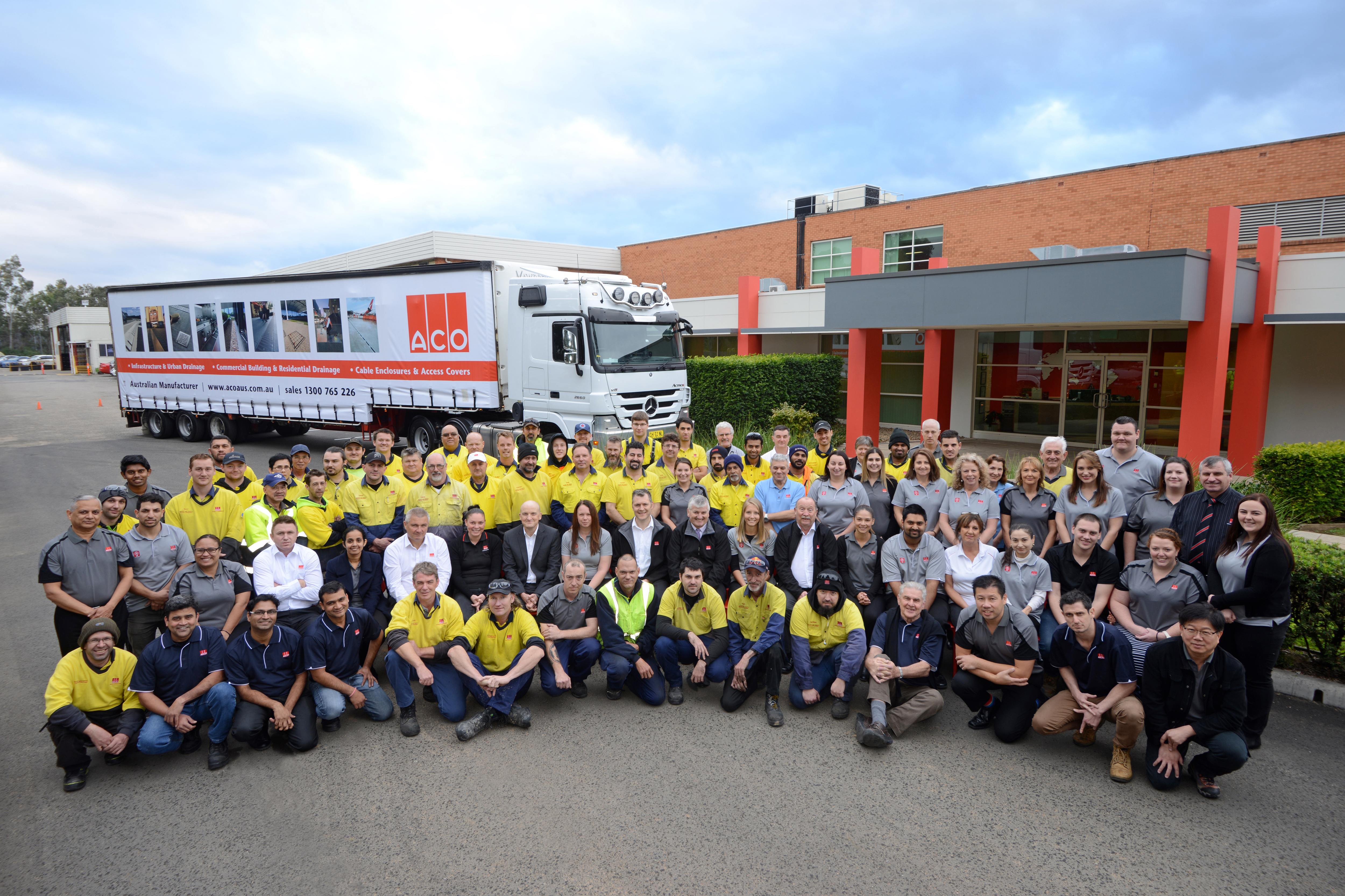 a large group of people looking at camera with a building and truck behind